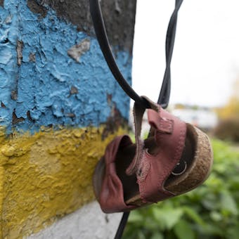Close-up foto van een kinderschoentje handend aan een muur waar de Oekraïense vlag op geschilderd is.