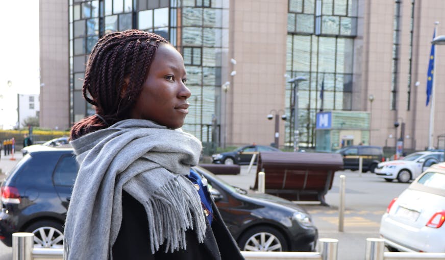 Yvonne loopt door Brussel met een oranje map onder haar arm met haar speech erin. Ze draagt een dikke sjaal en een zwarte jas.