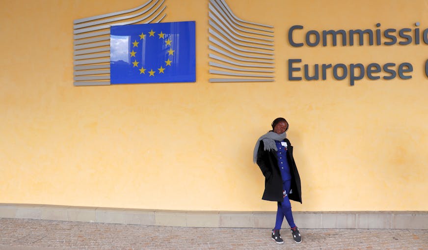 Yvonne staat voor de muur met een groot logo van het Europese Comité en de Europese vlag.