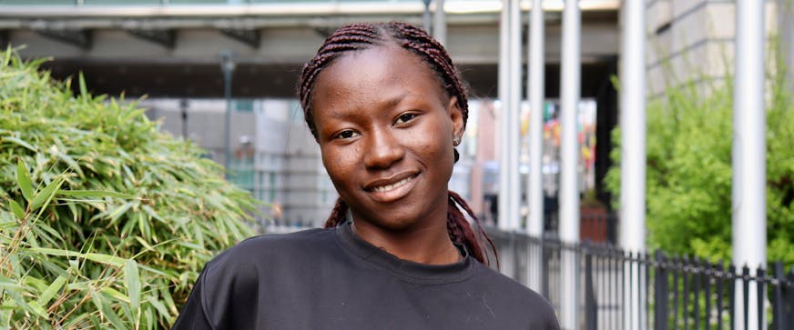 Yvonne (17) uit Tsjaad staat voor een parlementsgebouw en kijkt lachend in de camera.