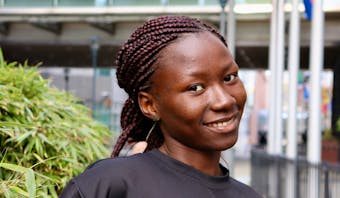 Portret van Yvonne (17 jaar) uit Tsjaad. Ze staat in Brussel voor een Europees parlementsgebouw en lacht in de camera.