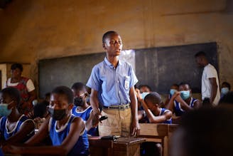 Kinderrechtenclubs - een jongen in een blauw uniform staat voor zijn bureau op een school in Ghana.