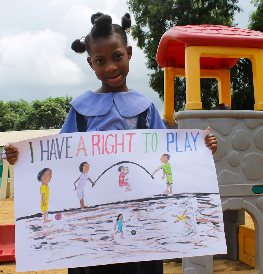 Een meisje uit het kinderdorp in Liberië houdt een tekening vast waarop staat: “I have the right to play.” Op de tekening zijn kinderen te zien met een springtouw.