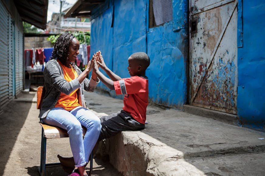 Een oudere zus en jonger broertje geven elkaar een high five in Nairobi, Kenia.