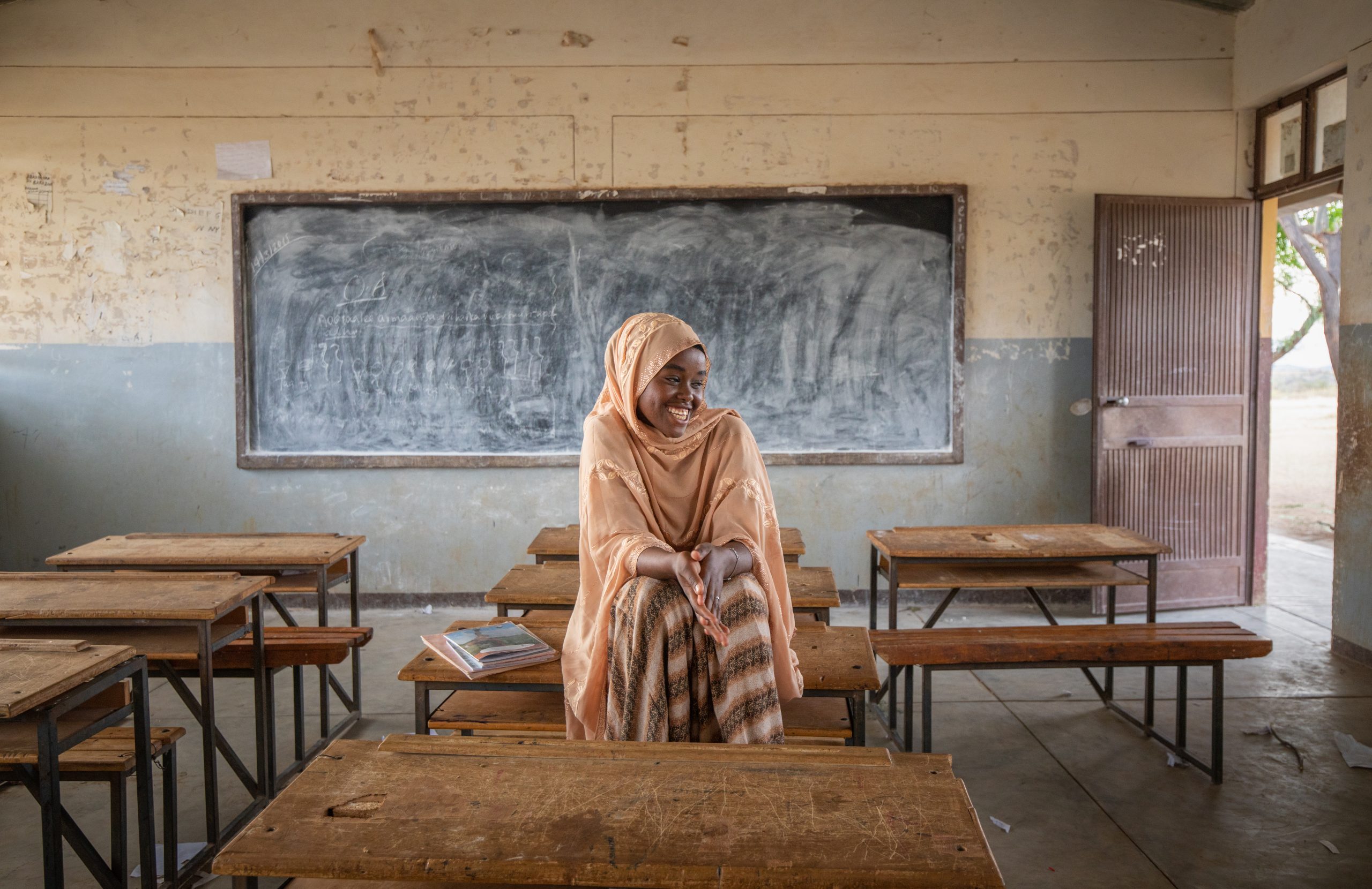 Ethiopische jongevrouw met hoofddoek zit op schoolbank