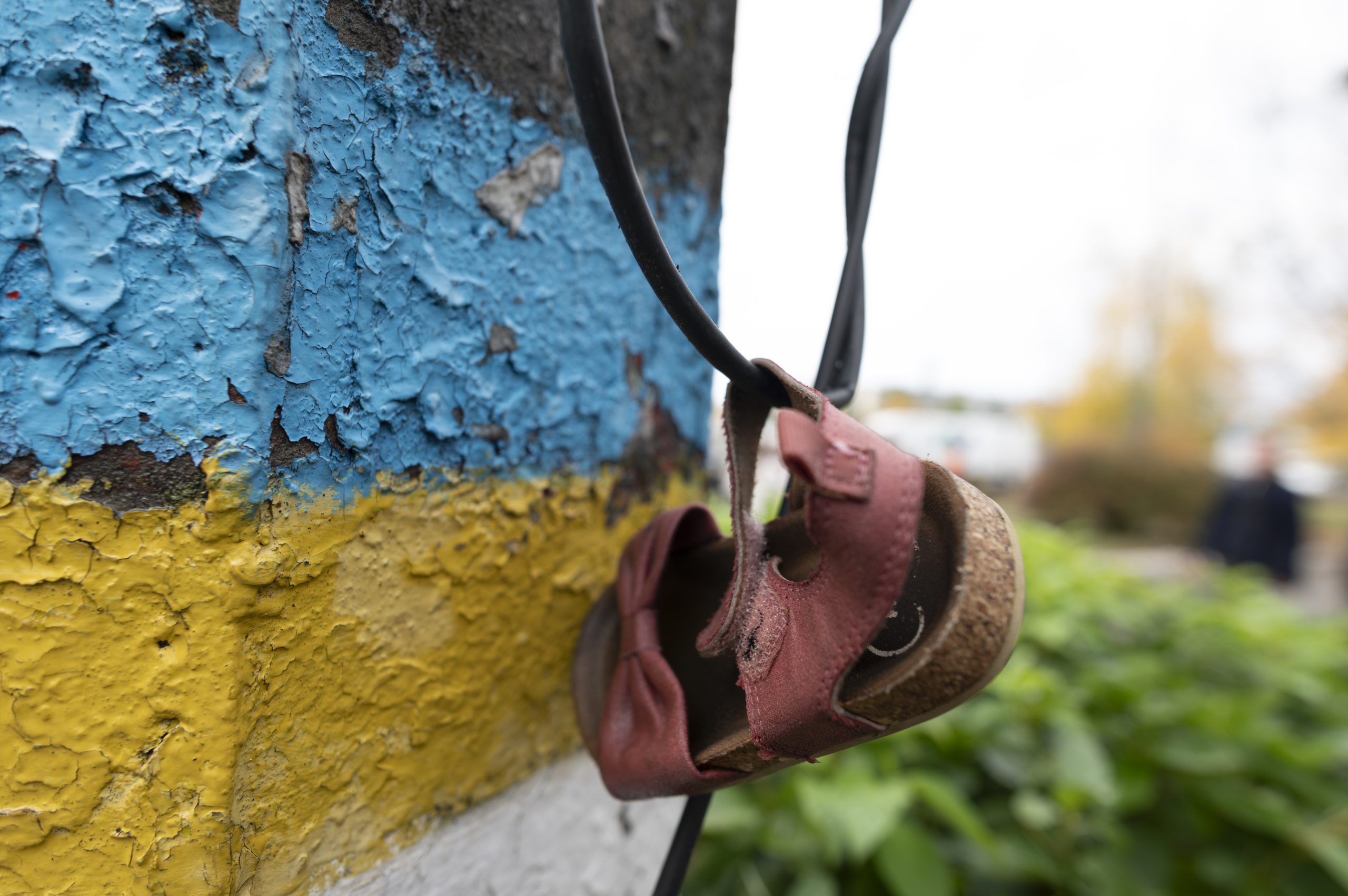 Close-up foto van een kinderschoentje handend aan een muur waar de Oekraïense vlag op geschilderd is.