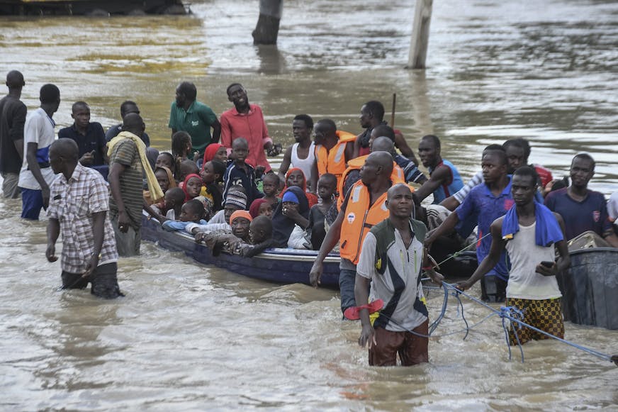 Mensen die door overstromingen zijn getroffen in Nigeria worden met een militaire boot door het water geholpen.