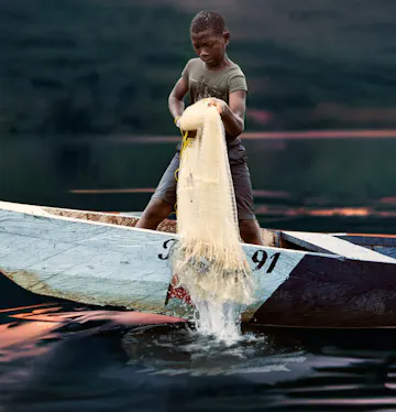 Jongen in de kinderarbeid bij het Voltameer in Ghana. Hij haalt een net op vanuit een kano.