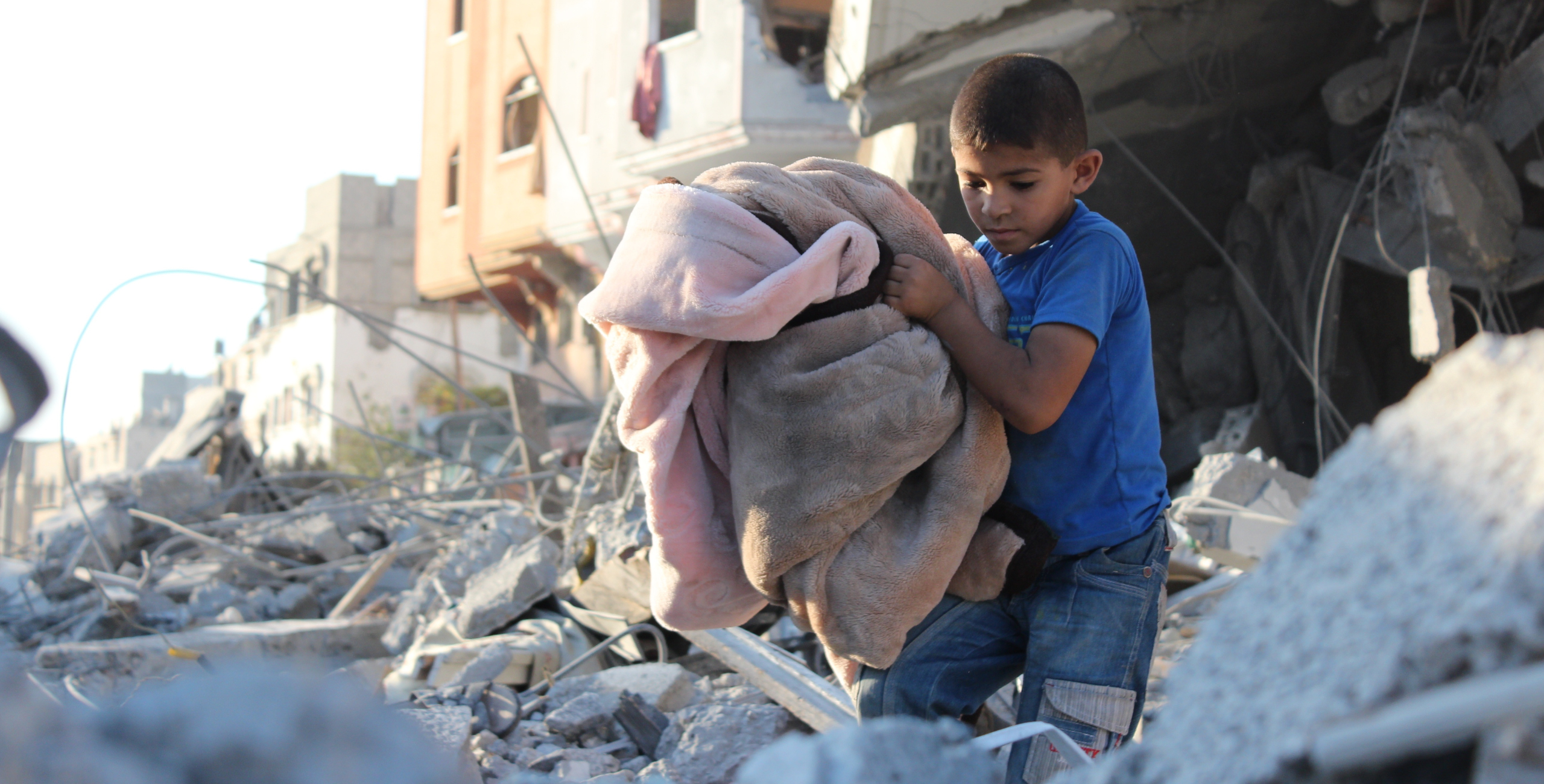 Jongen in Gaza loopt met dekens door de brokstukken en het puin