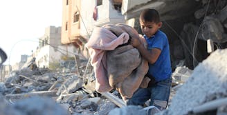 Jongen in Gaza loopt met dekens door de brokstukken en het puin
